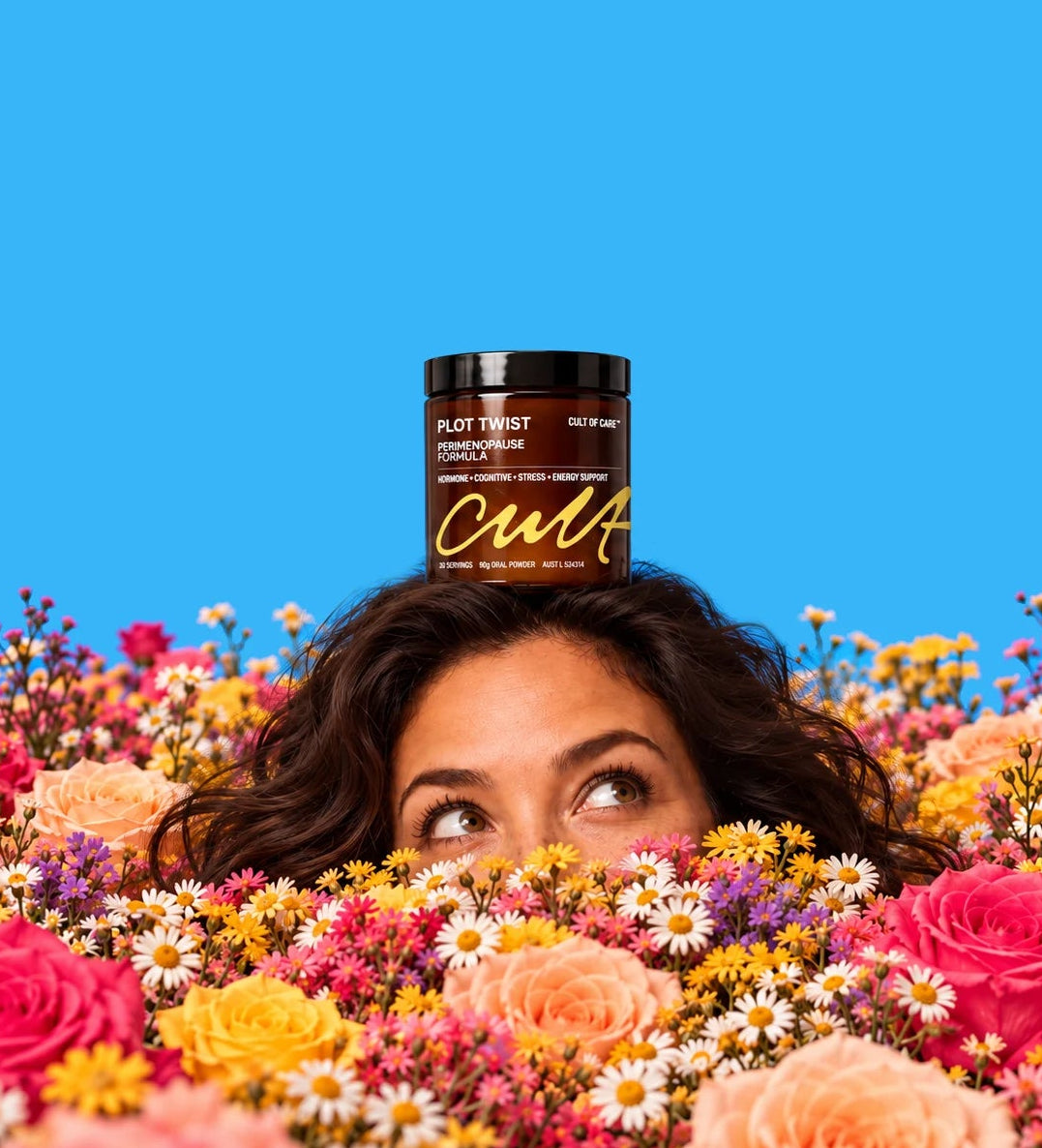 A woman with dark curly hair peeks over a dense bed of colorful flowers, with a jar of Cult of Care Plot Twist Perimenopause Formula placed on top of her head against a solid bright blue background.