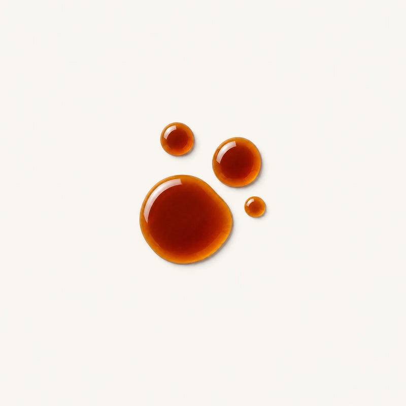 Three glossy amber-brown liquid droplets of Potassium iodide on a plain off-white background.